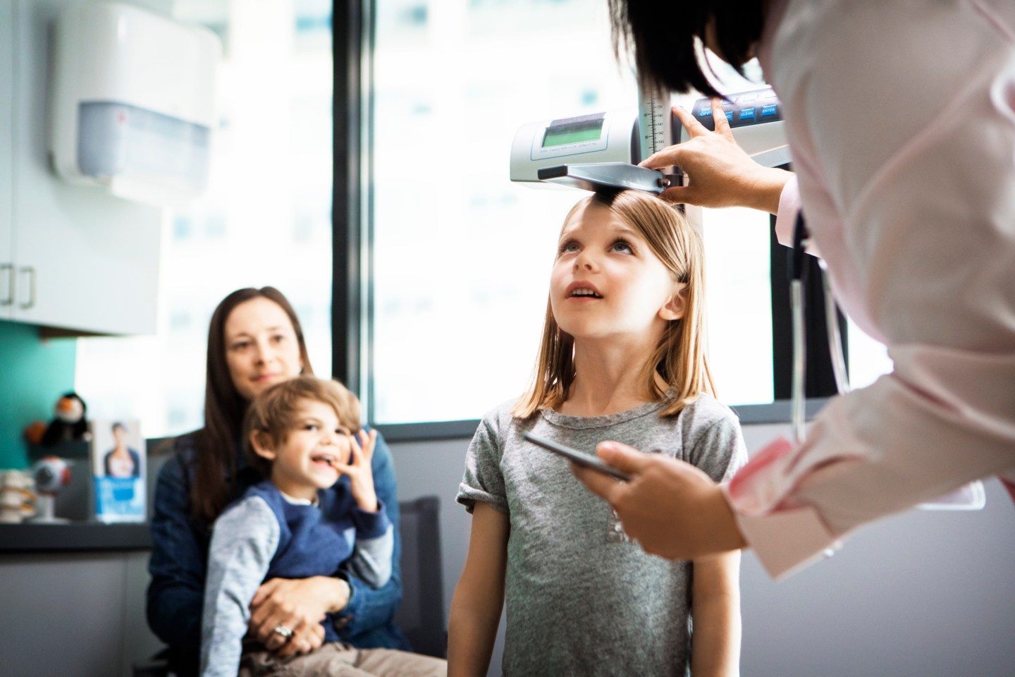 Doctor measuring girls height while family sitting at clinic