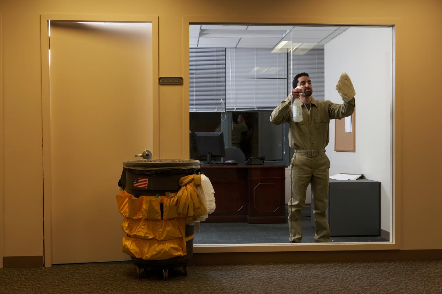 Janitor in office late at night, cleaning window