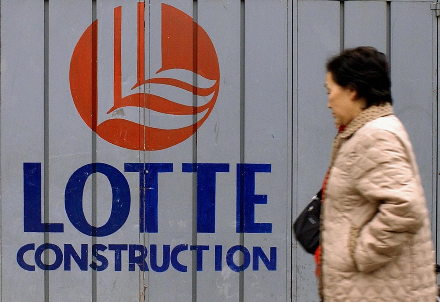 A woman walks past a logo of Lotte Group