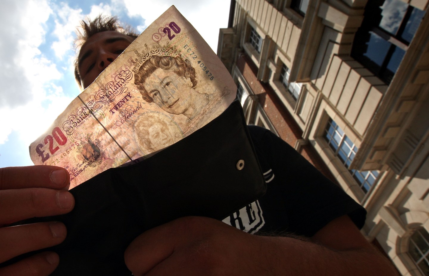 A man takes a 20 pound note from his wallet outside a bank in London.