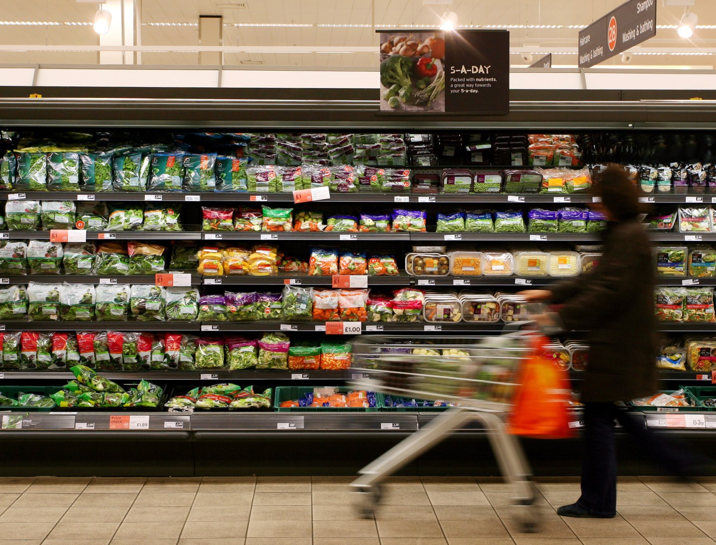 A customer walks past the pre-packed salads and vegetables o