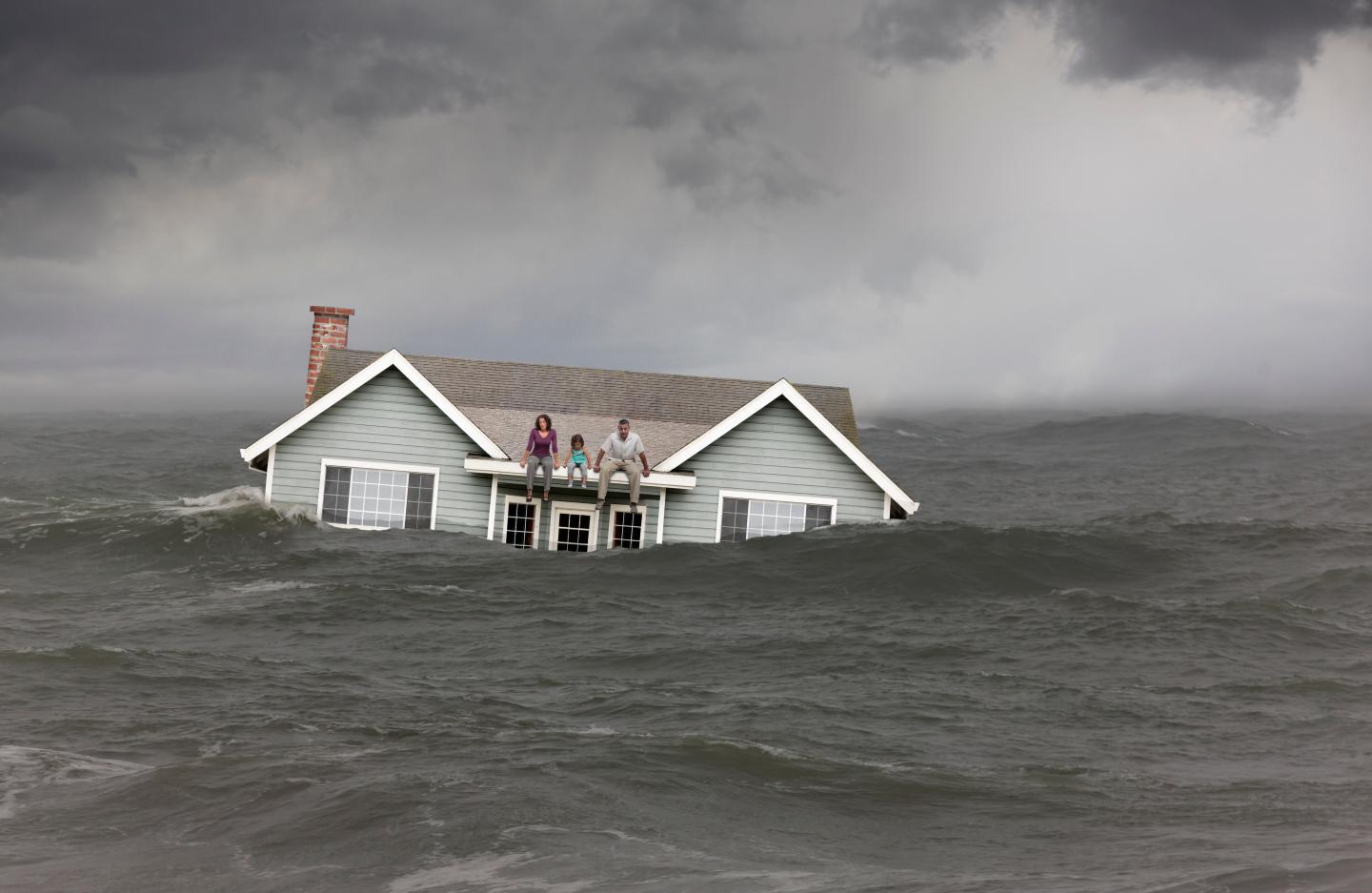 Family sitting on roof of house floating in sea