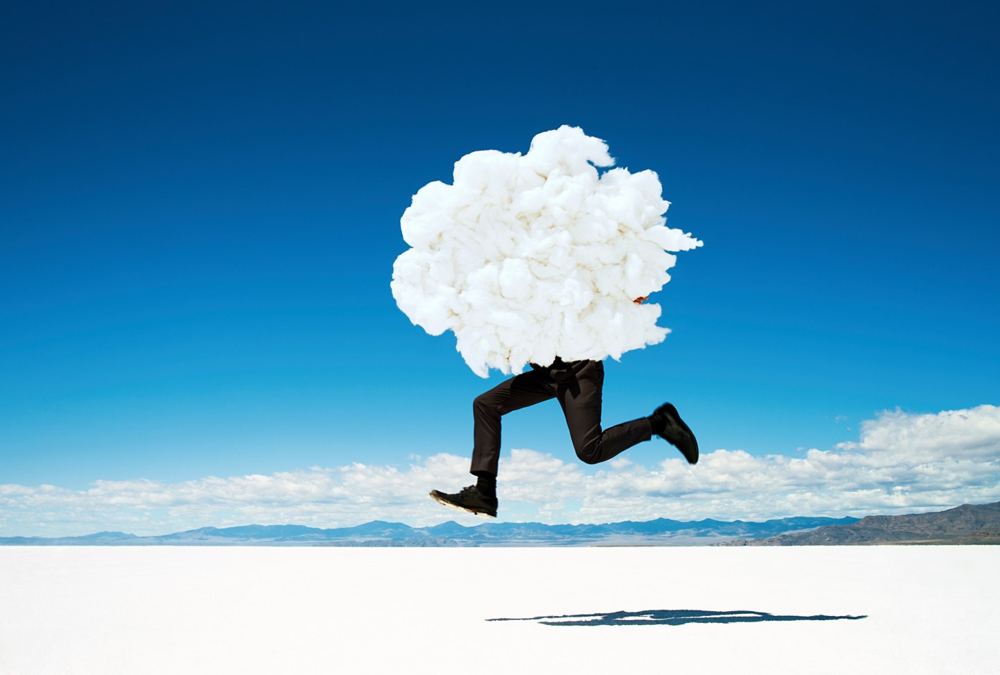 Man leaping on salt flats holding giant cloud.