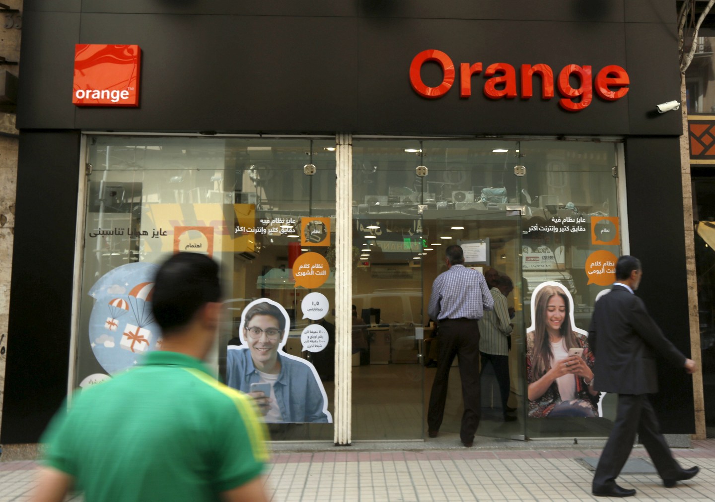 People walk past a new shop of French telecom operator Orange, which was previously known as Mobinil, in Cairo