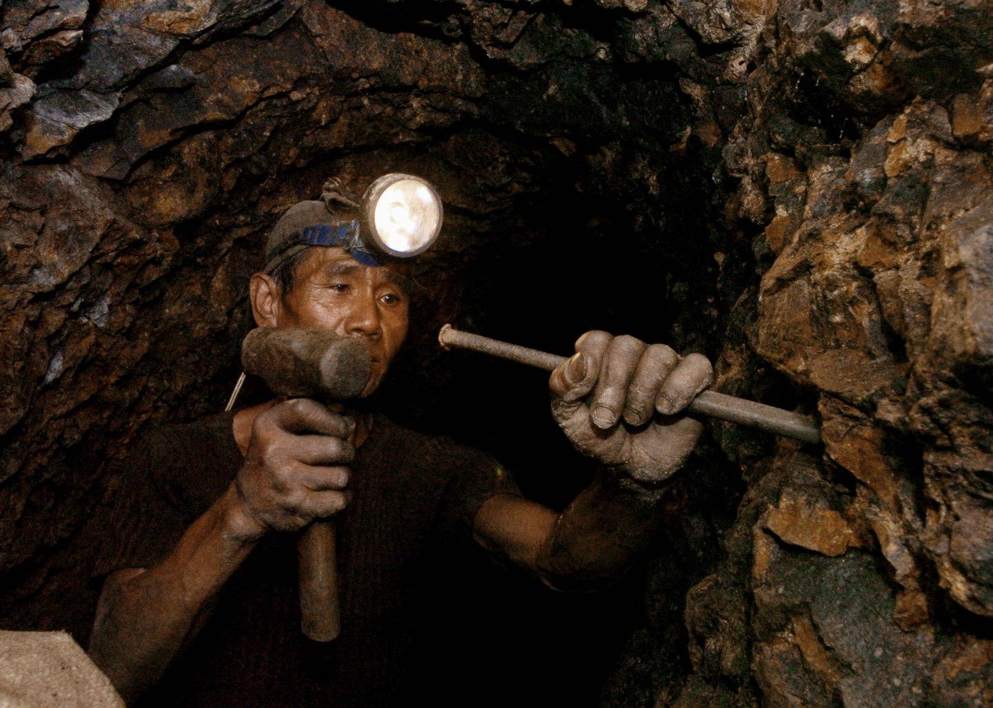 A worker hammers gold ore inside a mine