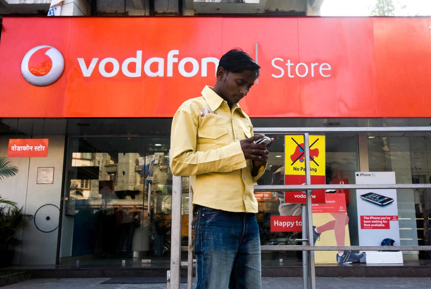 A pedestrian using a mobile phone stops outside a Vodafone s
