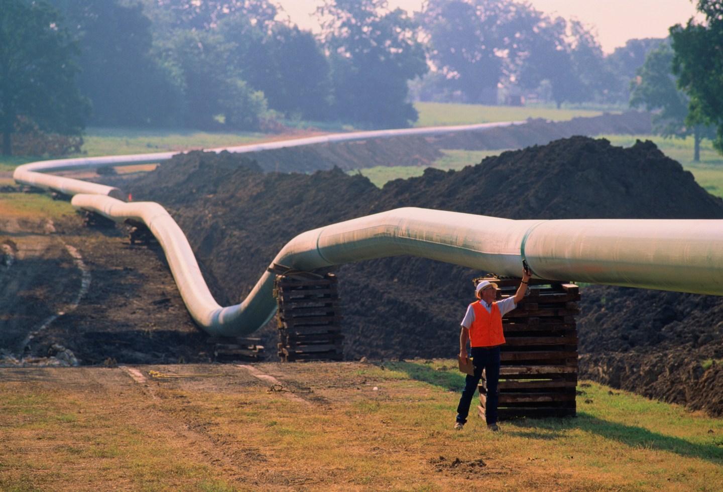 Worker checking welds on natural gas pipeline running through field