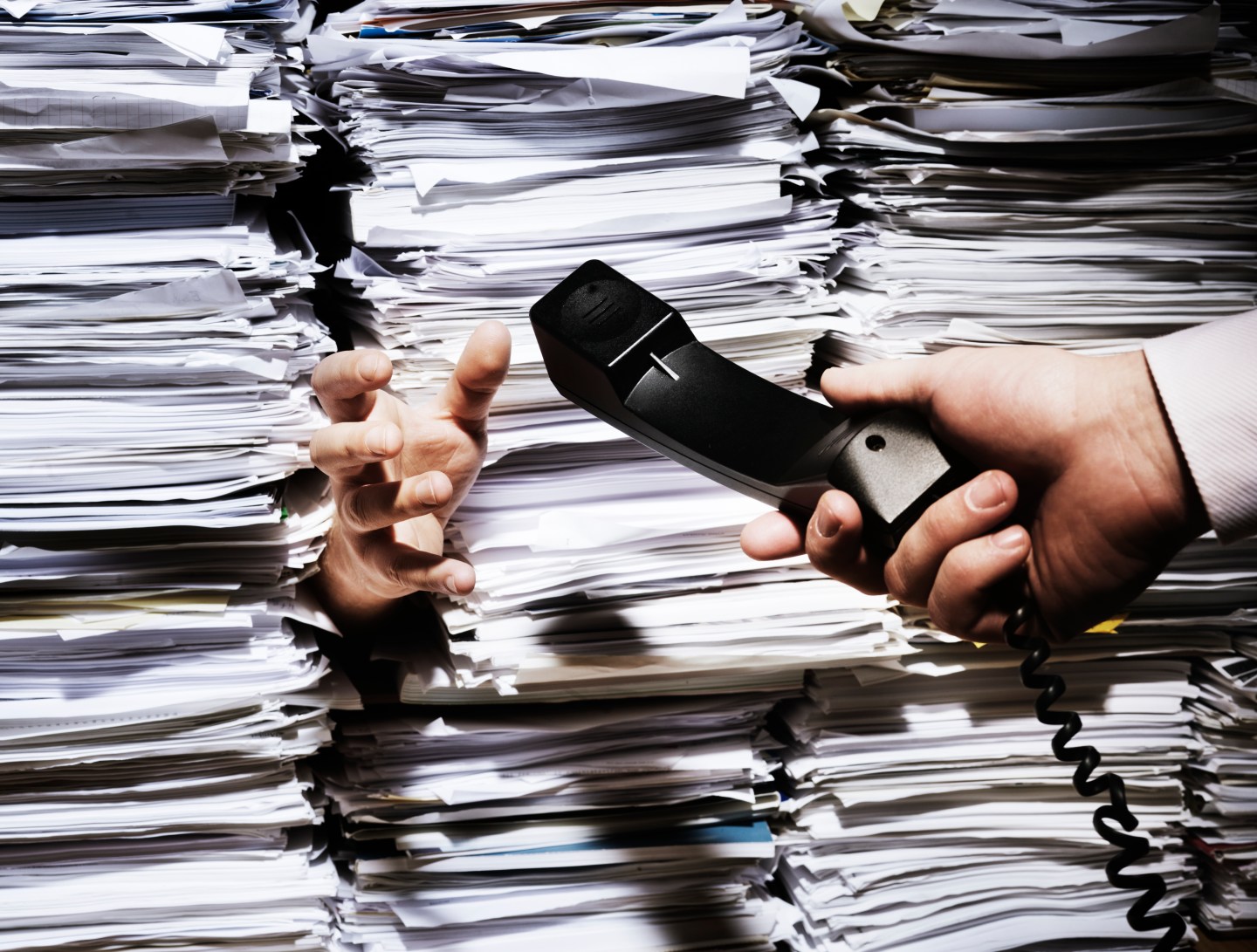 A hand sitcking out from a pile of papers recieving a phone call.