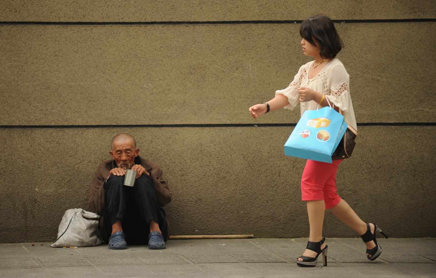 A man begs on a street as a woman passes