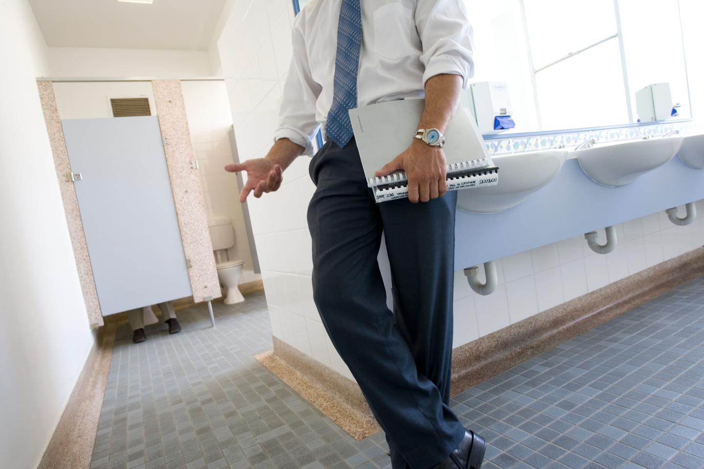 Businessman holding file leaning against sink in office toilets
