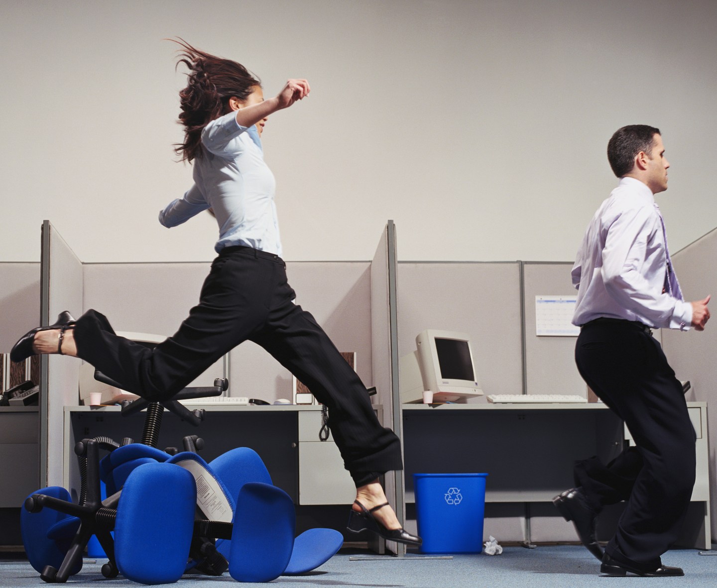 Man and woman running through office, hurdling chairs