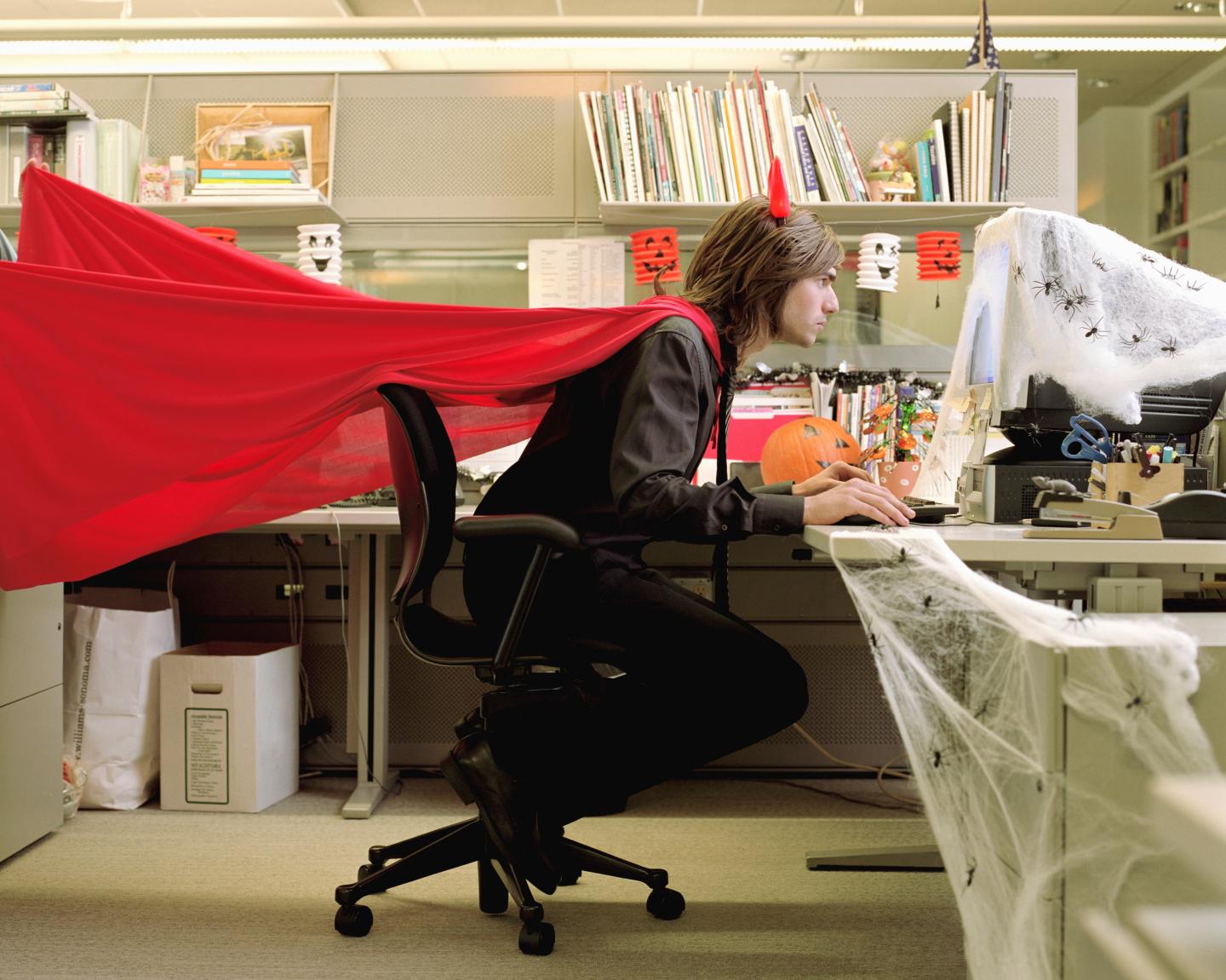 Man wearing devil costume working in cubicle decorated for Halloween