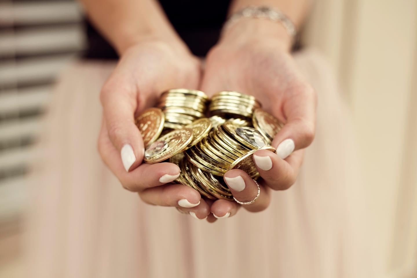 Young woman with handful of gold coins, focus on hands