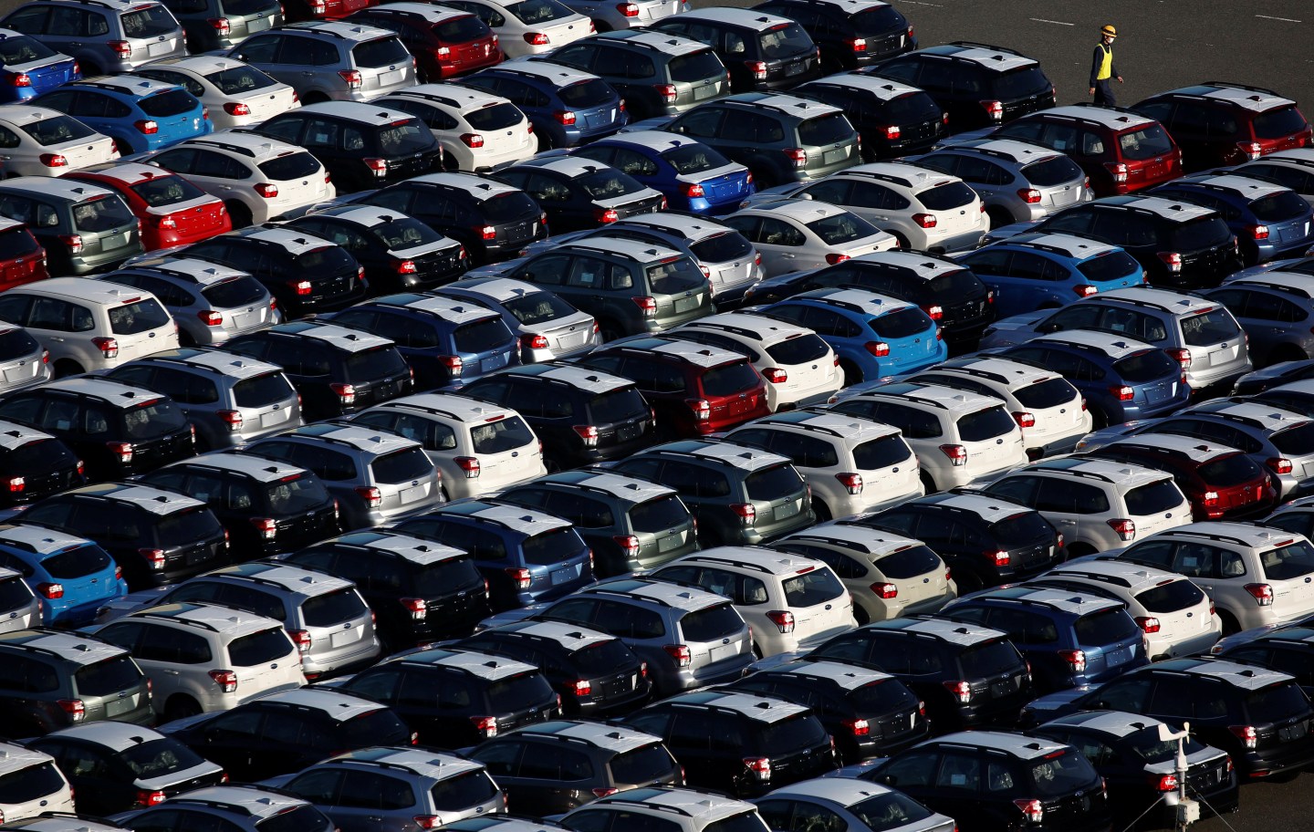 A worker walks past newly produced cars at an industrial port in Kawasaki