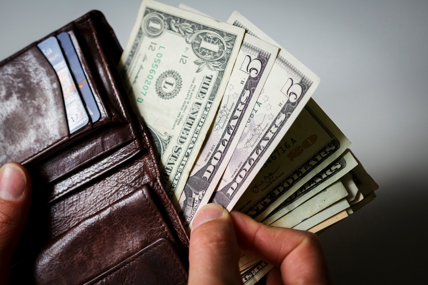 A man hold a wallet, filled with dollar bills.