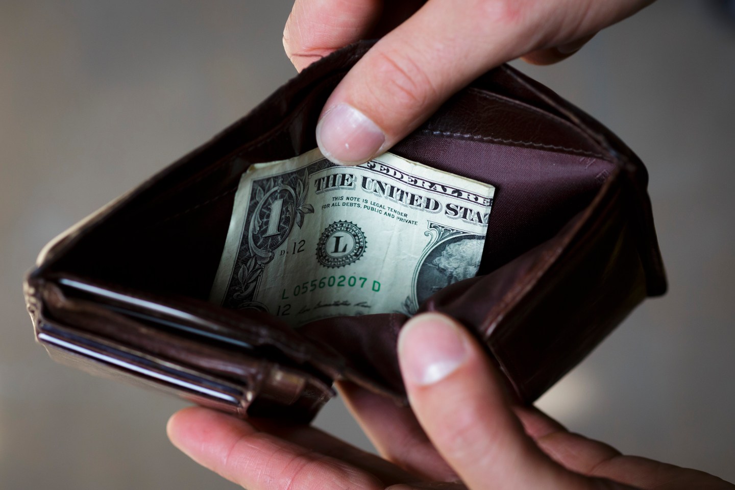 A man holds a wallet, filled with a one dollar bill.