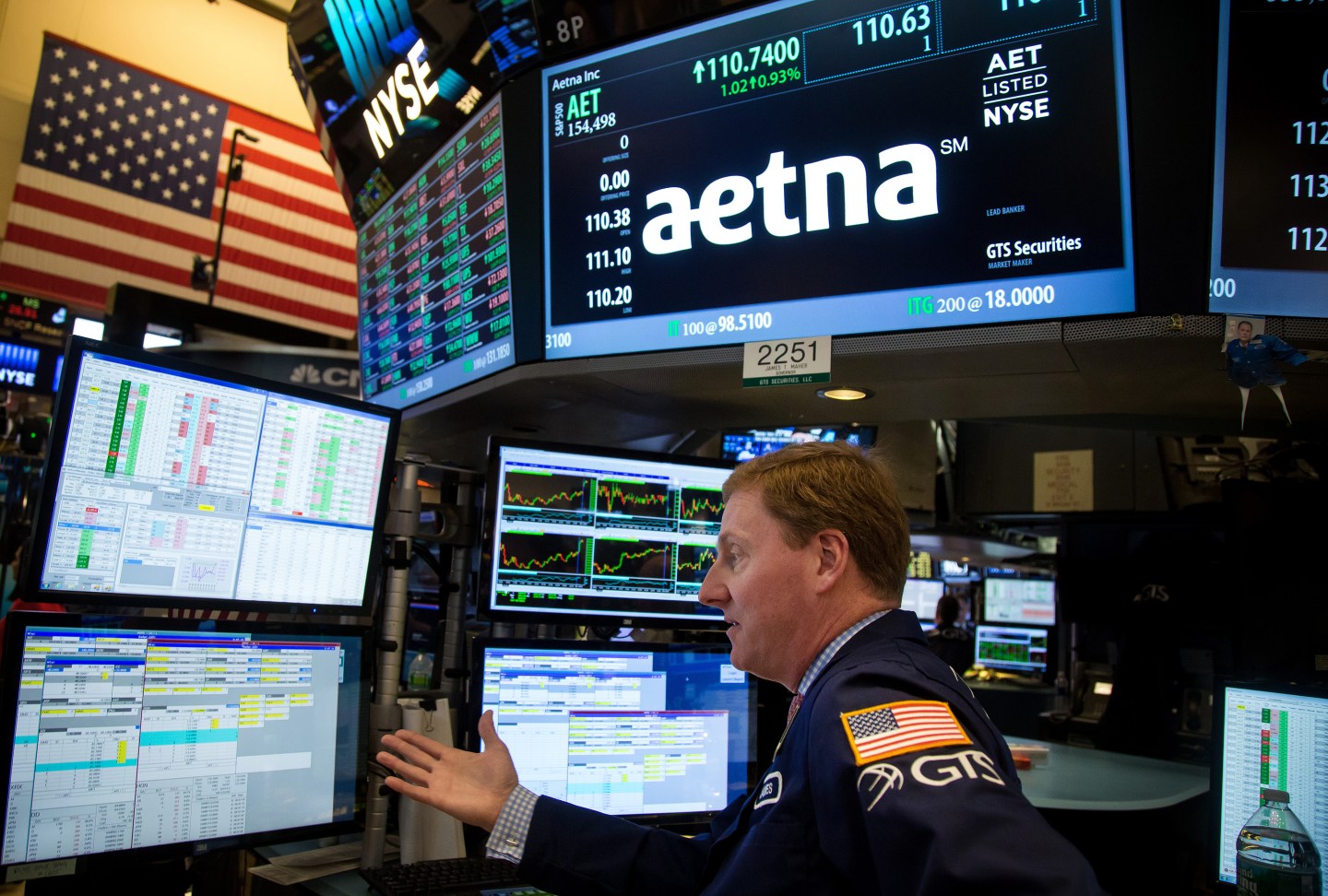 A trader works beneath a monitor displaying Aetna signage on the floor of the New York Stock Exchange.
