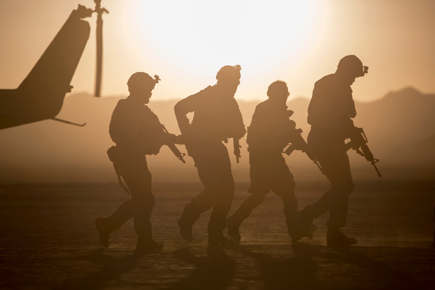 Silhouette of soldiers near helicopter in desert landscape