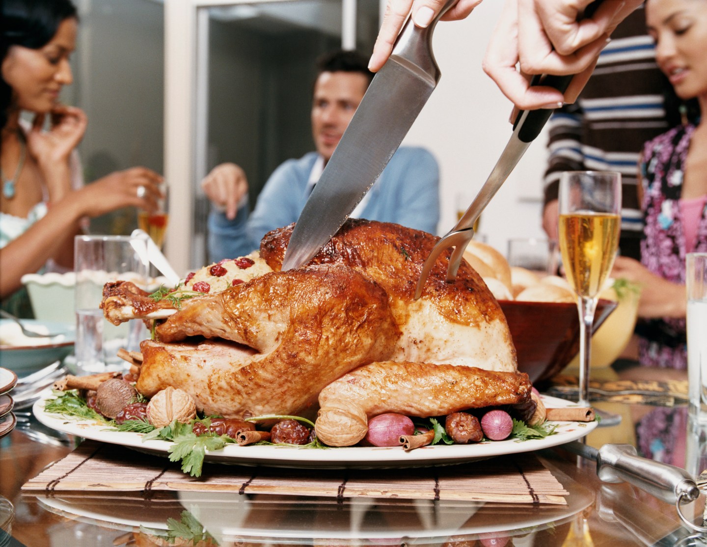 Small Group of Friends Sit Round a Dining Table While a Thanksgiving Turkey is Cut