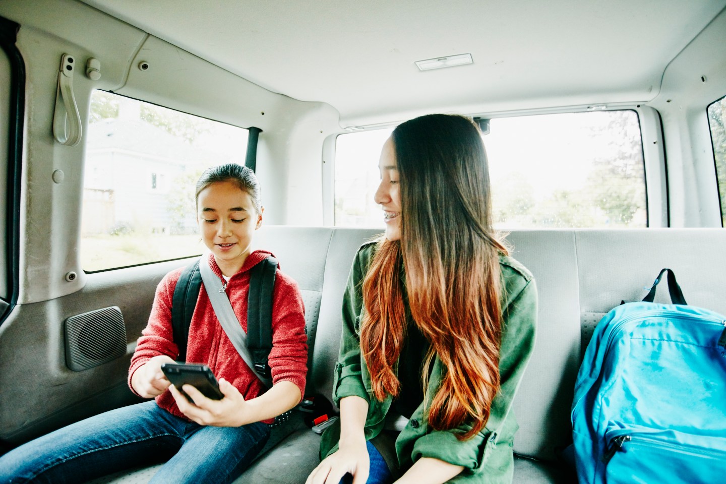Sisters looking at smartphone in backseat of van