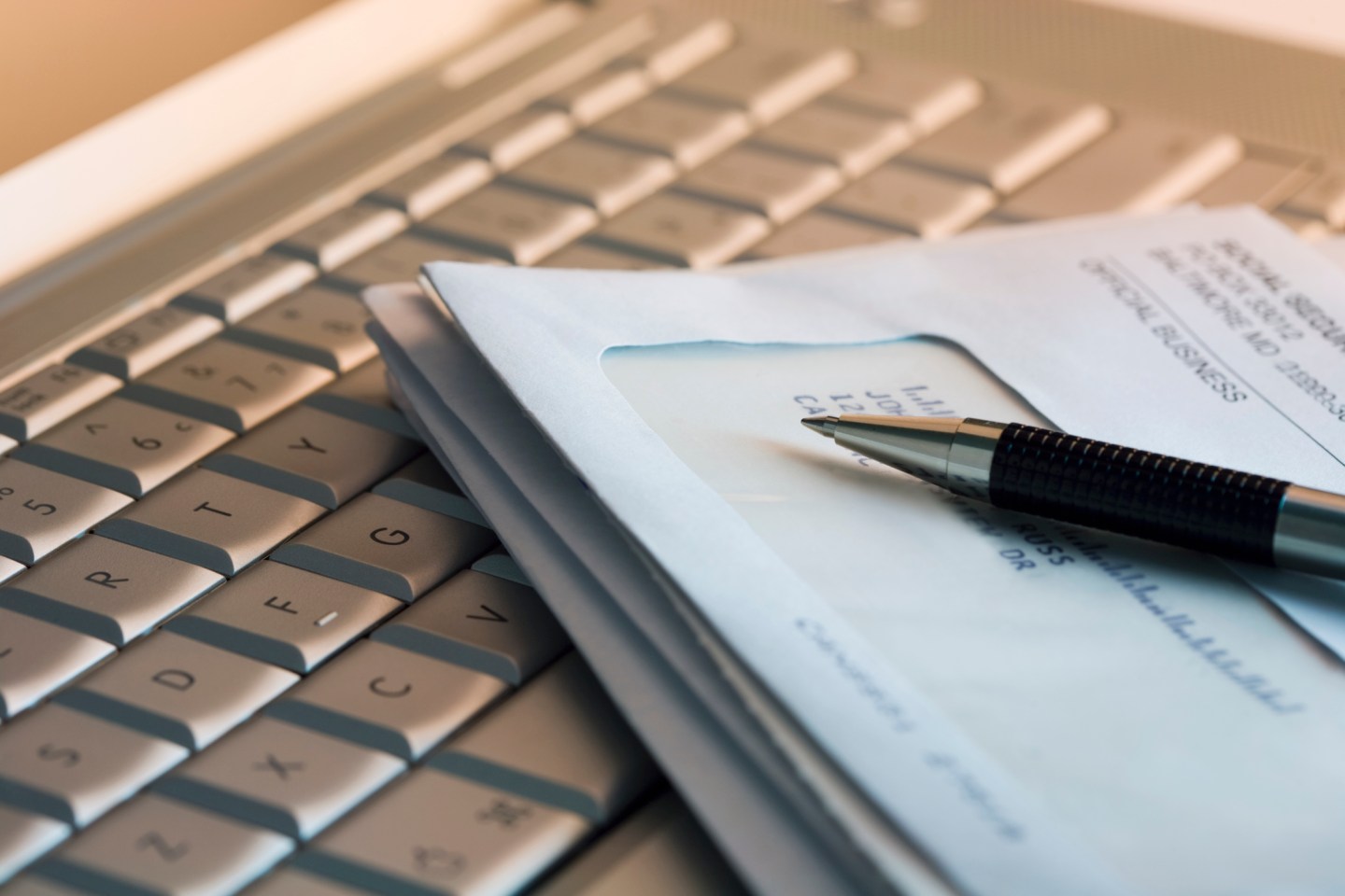 A laptop keyboard with a stack of bills and a pen on it