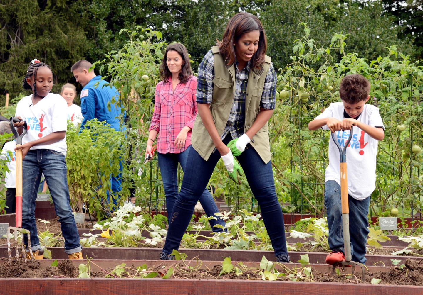 First Lady Michelle Obama encourages a youngster with a pitchfork as they harvest vegetables in the White House Kitchen Garden in Washington