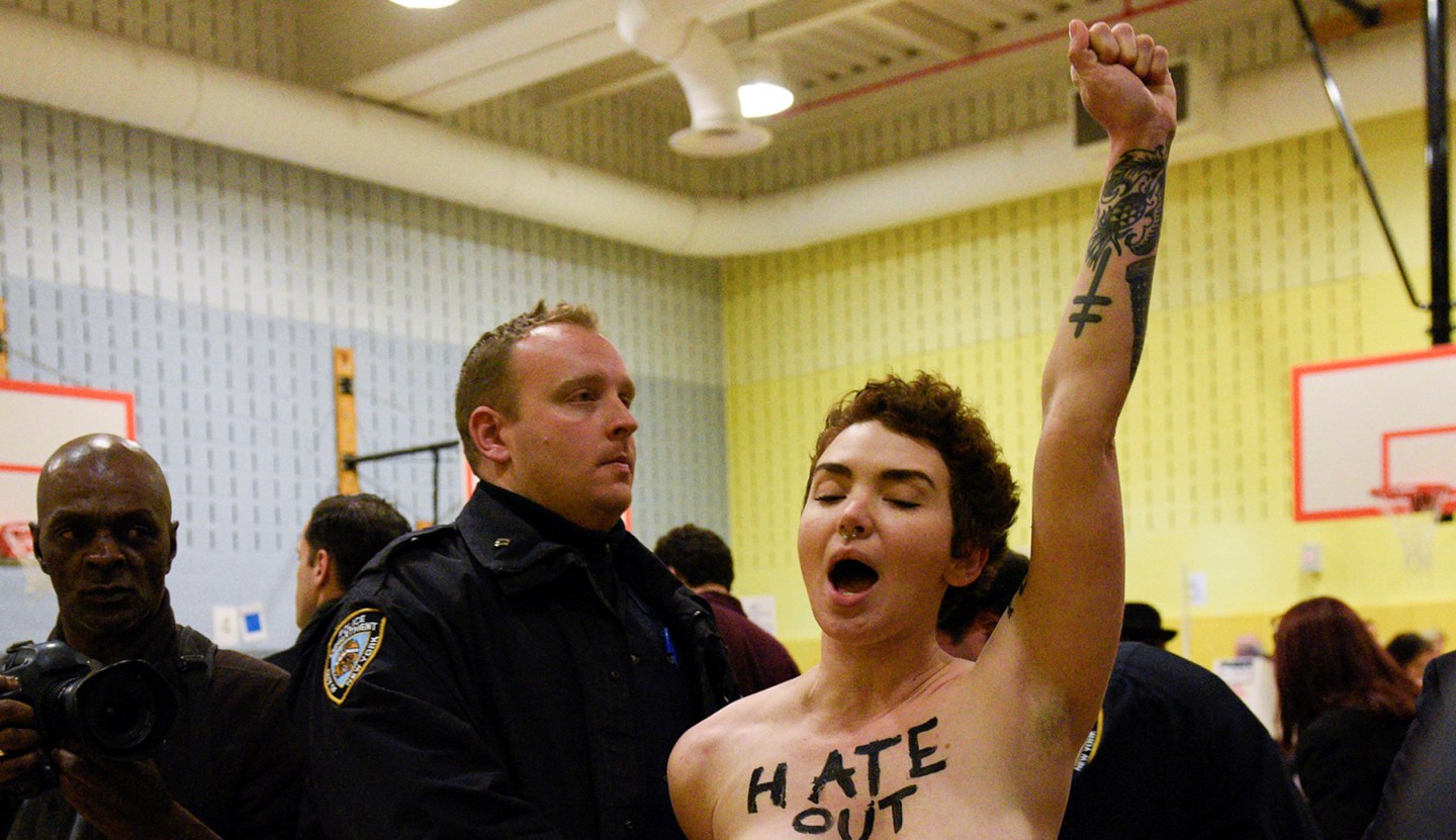 A topless protester shouting slogans is escorted out of polling station in New York