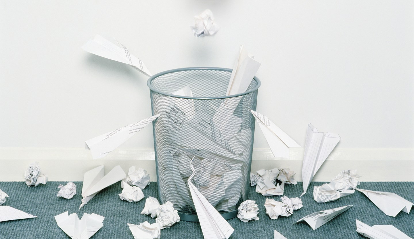 Man dropping crumpled paper in bin surrounded with paper aeroplanes