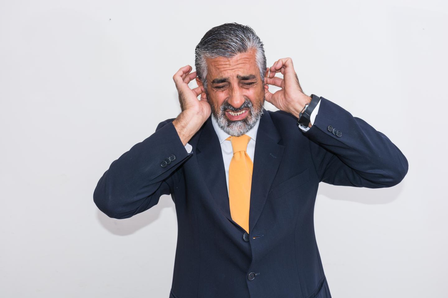 Businessman With Hands Covering Ears Against Wall
