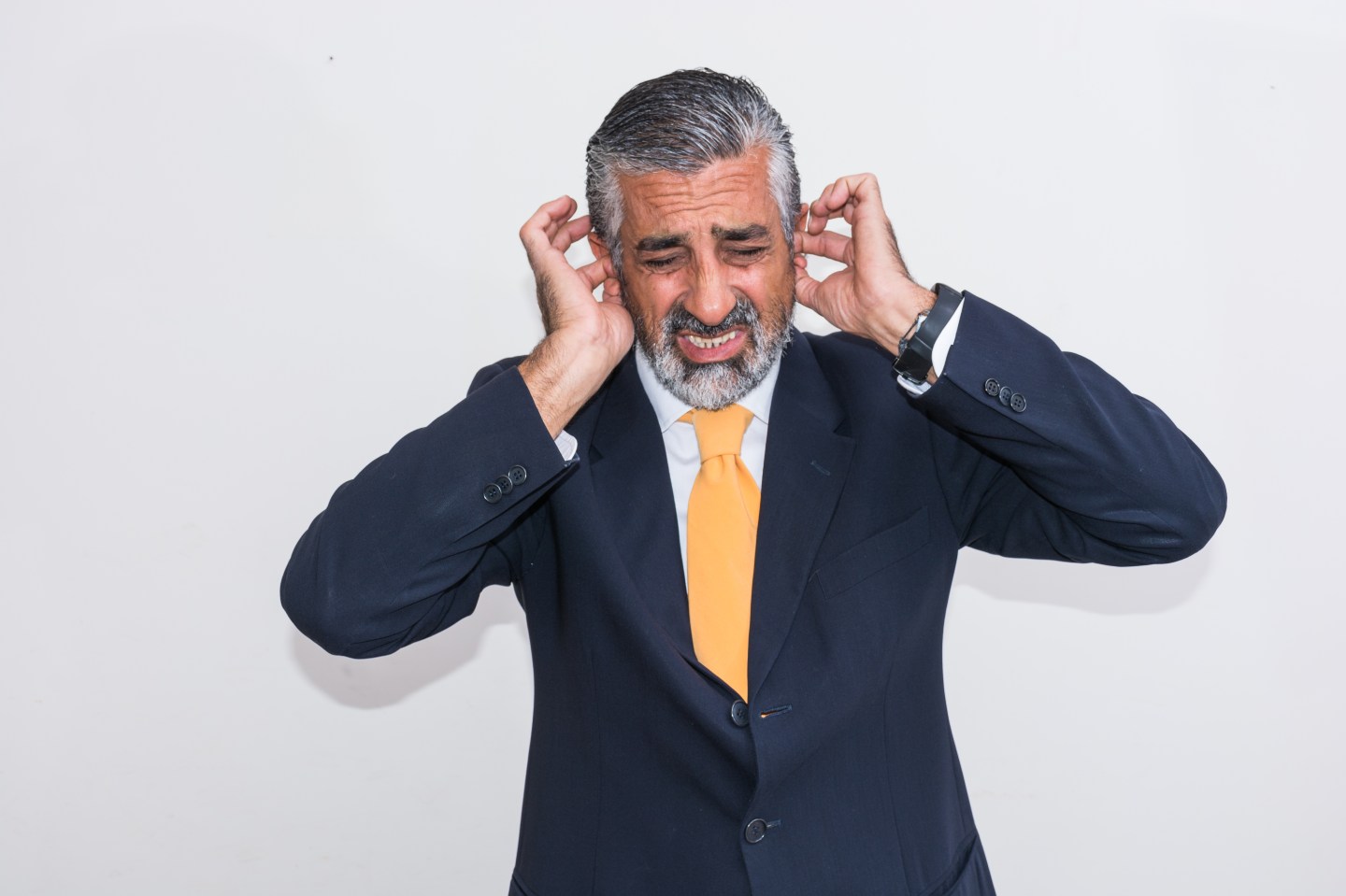 Businessman With Hands Covering Ears Against Wall