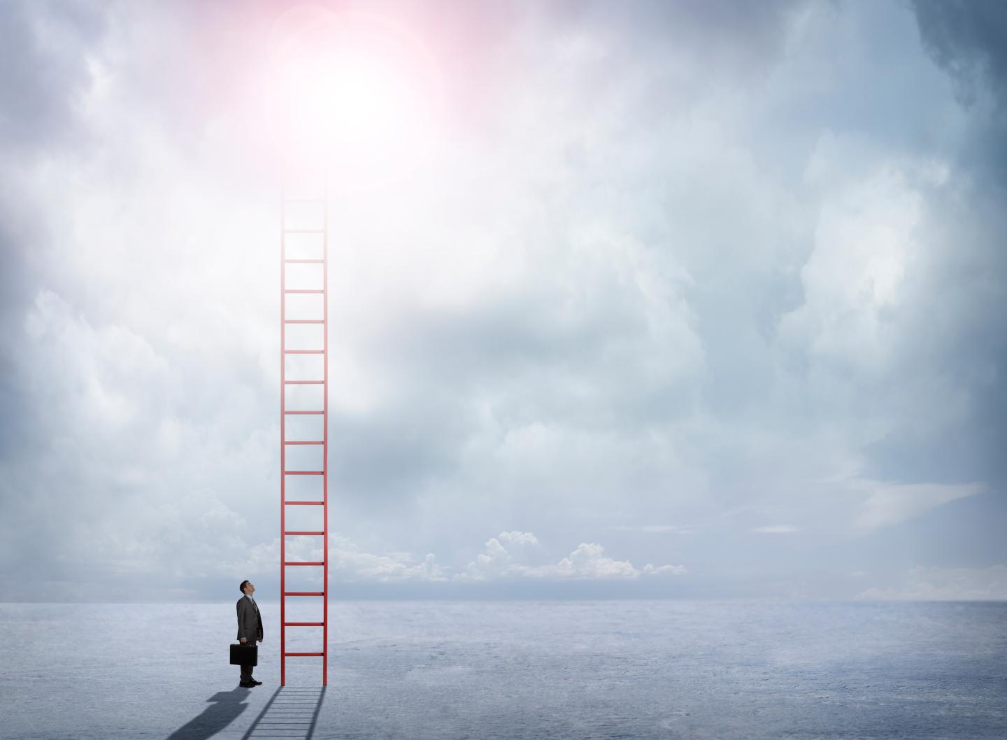 Businessman Looks Up At Red Ladder Extending Into The Clouds