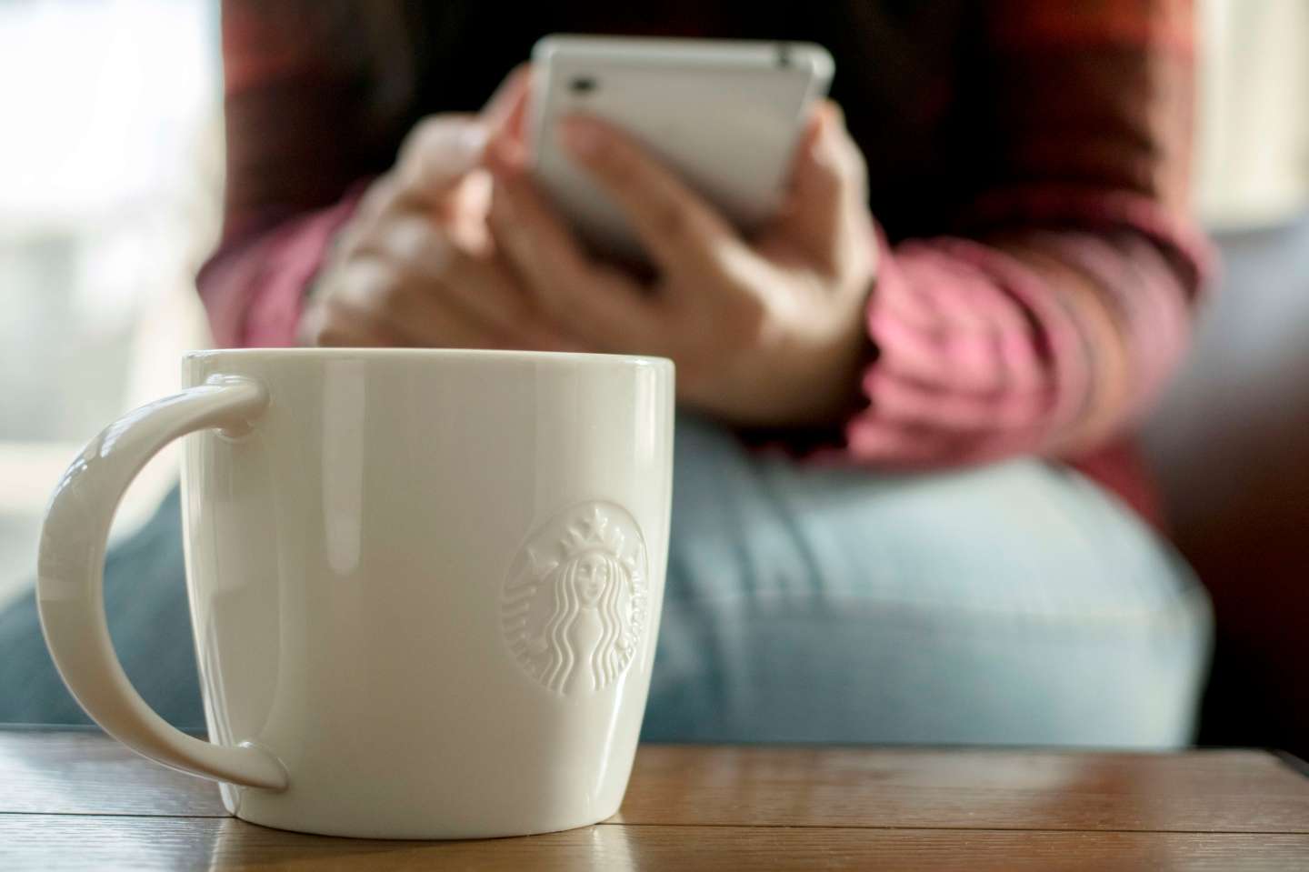 A Starbucks coffee cup on table, beside which a customer is