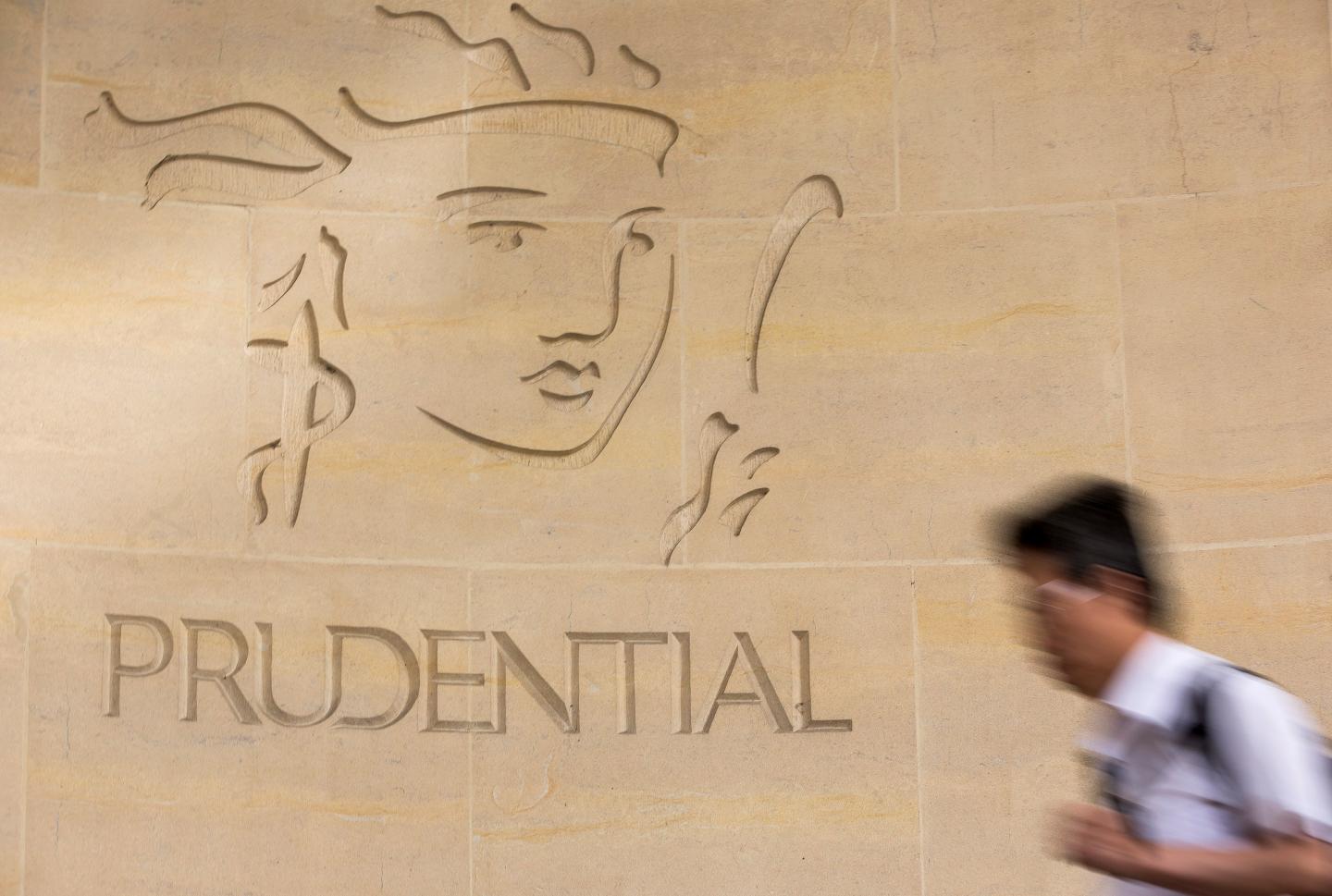 A pedestrian passes a logo outside Prudential Plc's headquarters in London, U.K., on Monday, Aug. 12, 2013.
