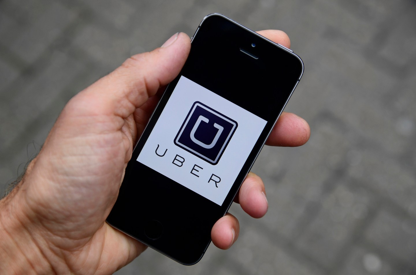 A photo illustration shows the Uber app logo displayed on a mobile telephone, as it is held up for a posed photograph in central London