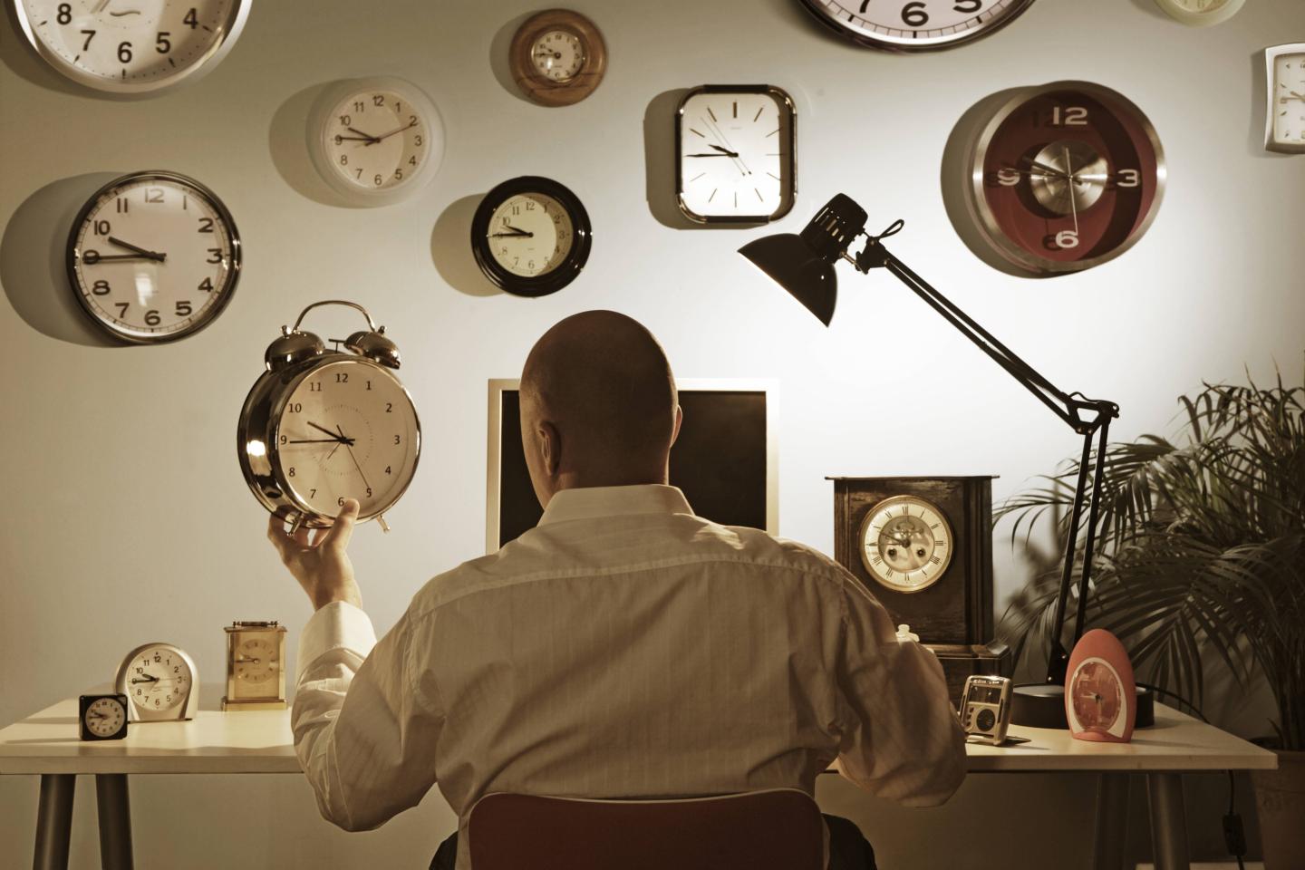 man sitting at desk surrounded by clocks
