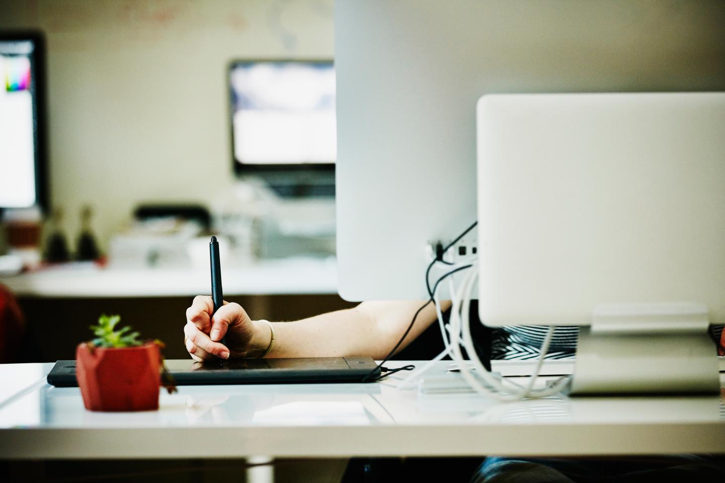 Designer drawing on tablet while working on project on computer in startup office