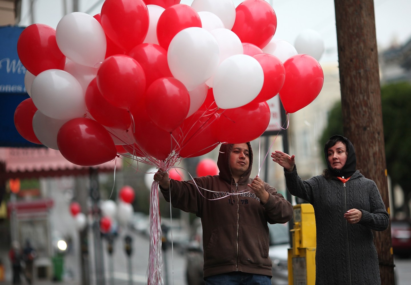 A man hands a balloon to a woman as he decorates Fillmore Street on Valentine's Day in San Francisco.