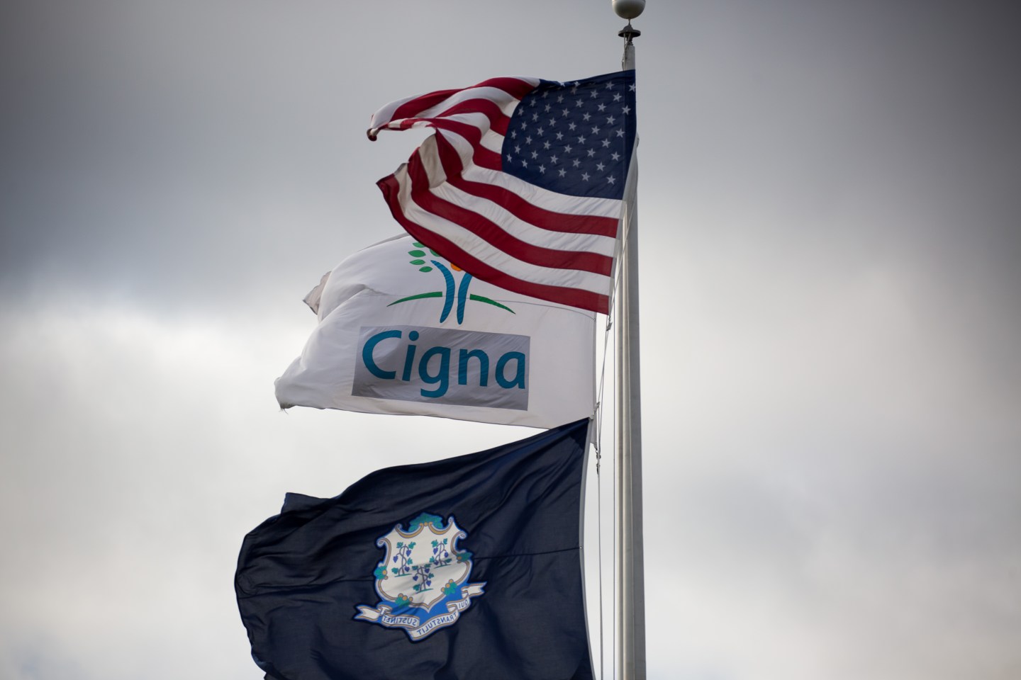 An American flag flies above a Cigna Corp. flag at the company's headquarters in Bloomfield, Connecticut, U.S., on Tuesday, Nov. 22, 2016. Anthem Inc.'s proposed $48 billion merger with Cigna Corp. could give the insurer the power to raise prices for employers both in the 14 states where it does business, as well as across the country, according to a witness in the U.S. government's lawsuit to block the deal. Photographer: Michael Nagle/bloomberg