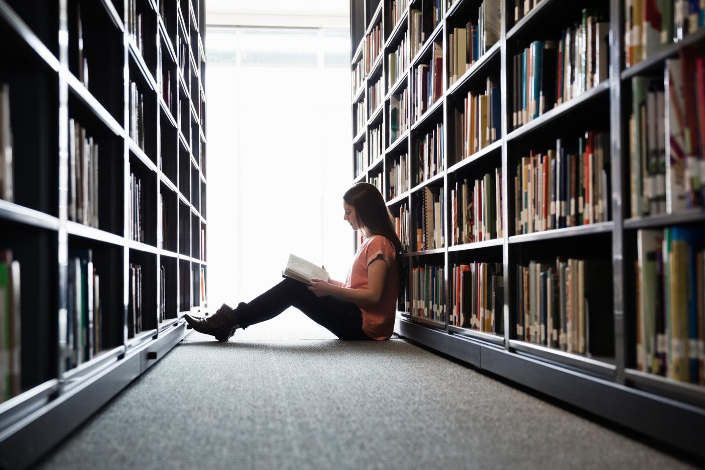 Female student sitting on library floor at college campus