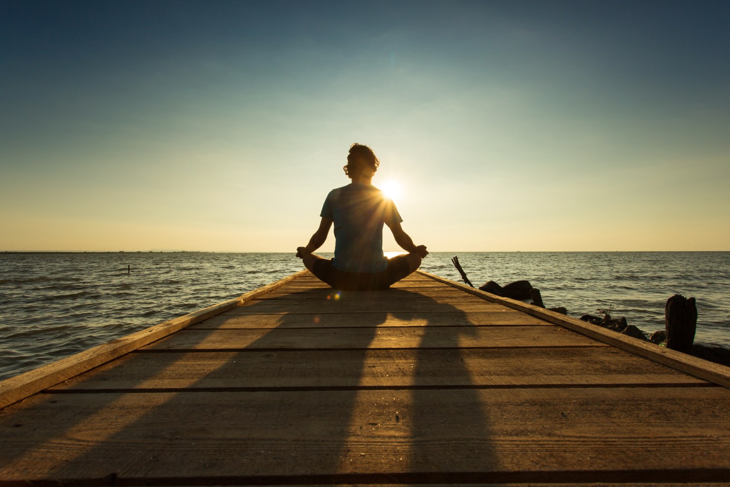 Joyful man meditating on pontoon over a lake at sunrise