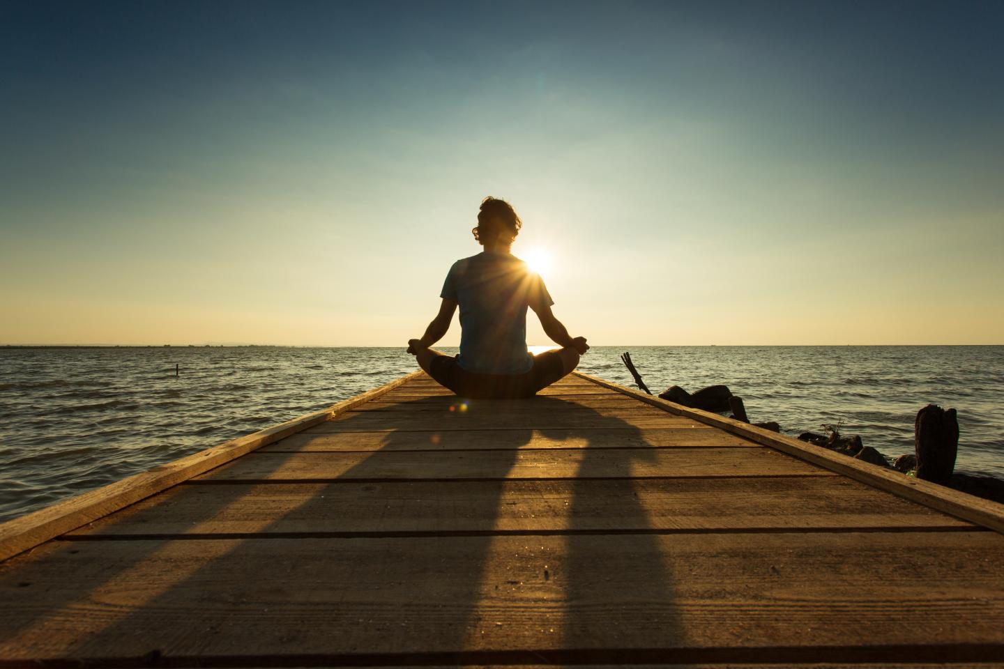 Joyful man meditating on pontoon over a lake at sunrise