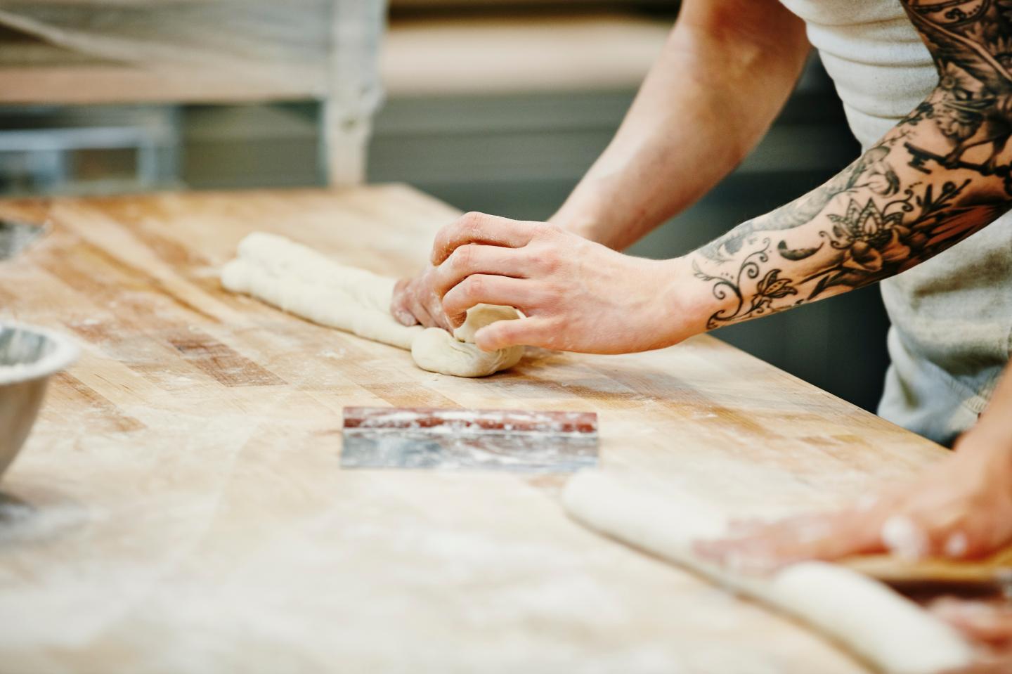 Bakers shaping dough for baguettes at table in bakery
