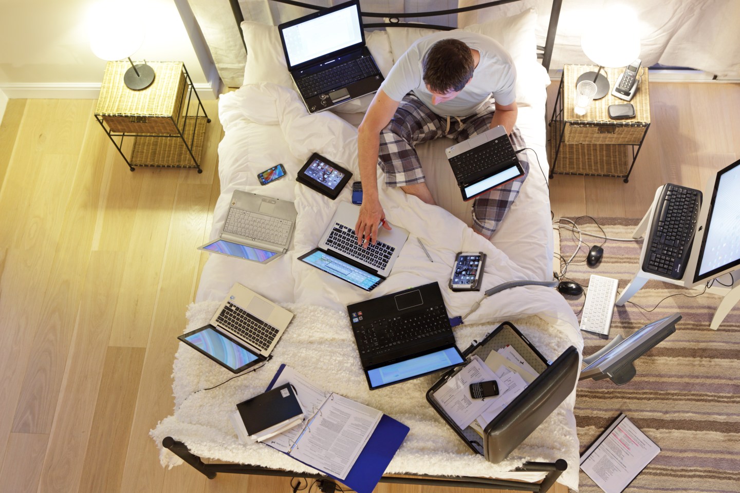 Man sat on bed surrounded by computers