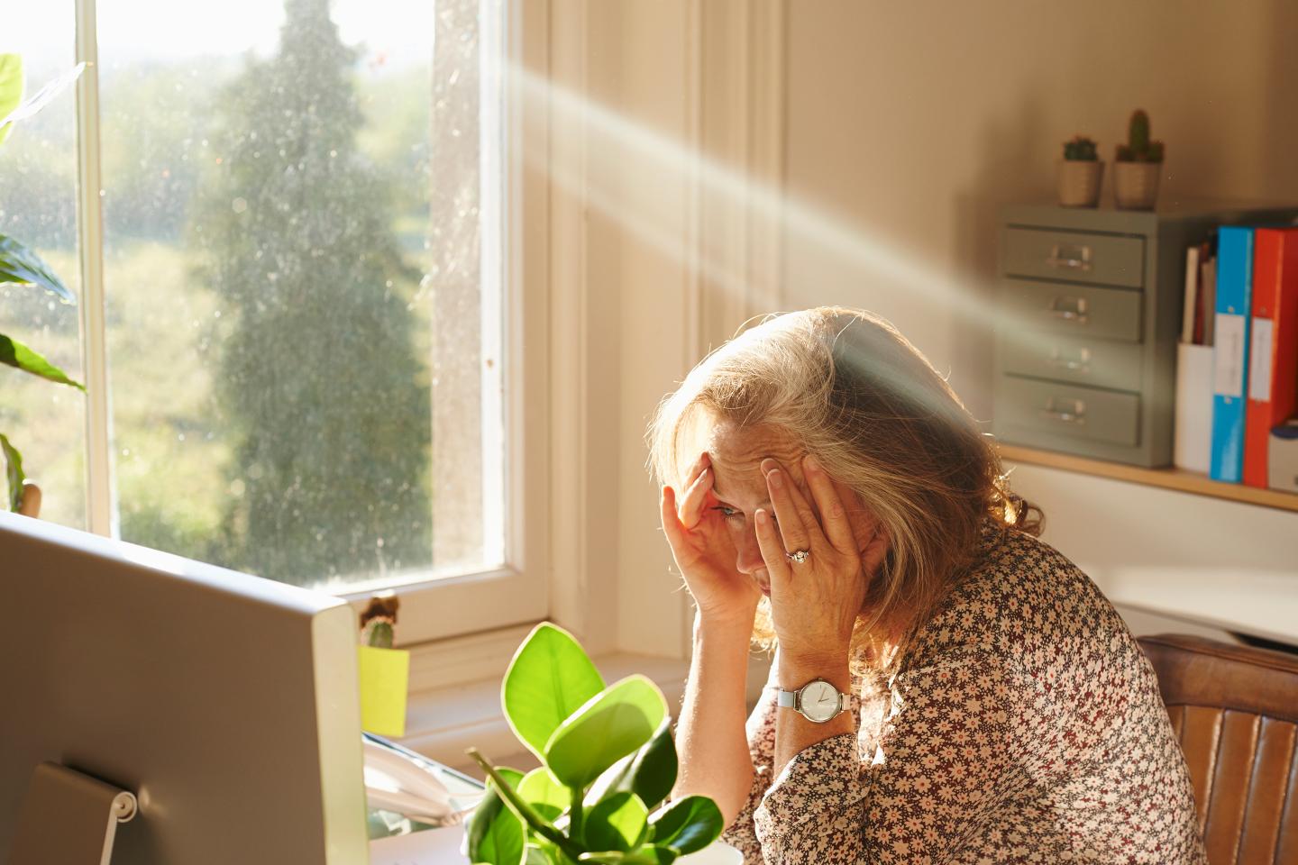 Stressed woman using computer in sunny home office