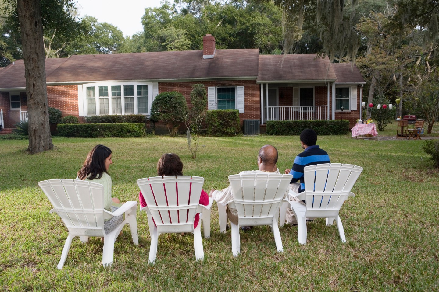 Rear view of four people in lawn chairs in backyard