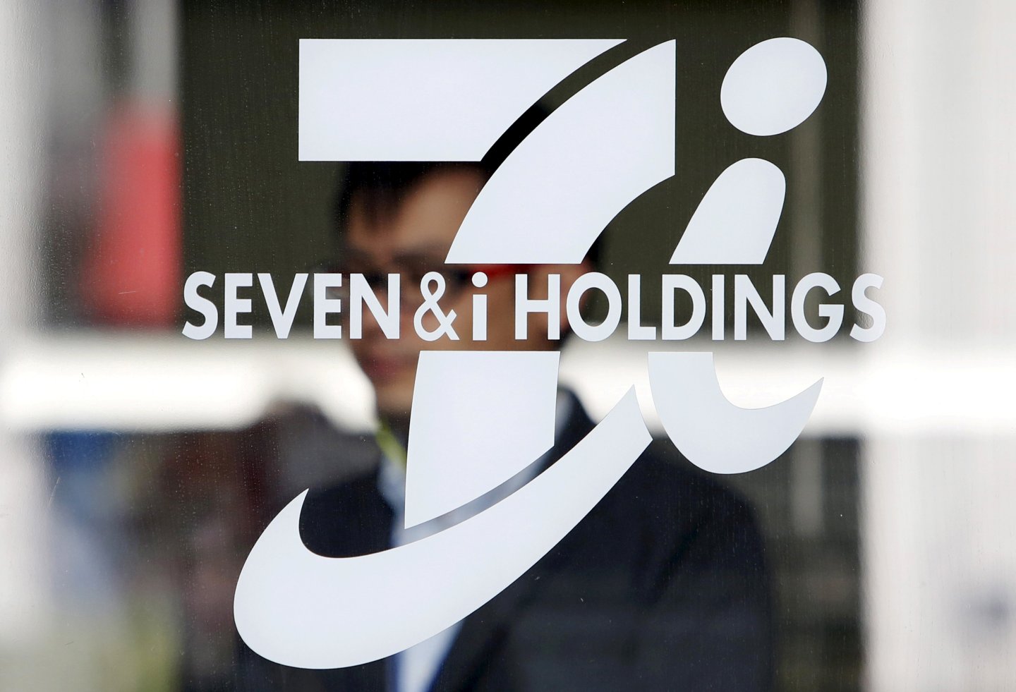 FILE PHOTO: A shopper is seen behind a Seven &amp; I Holdings' logo at a 7-Eleven convenience store in Tokyo