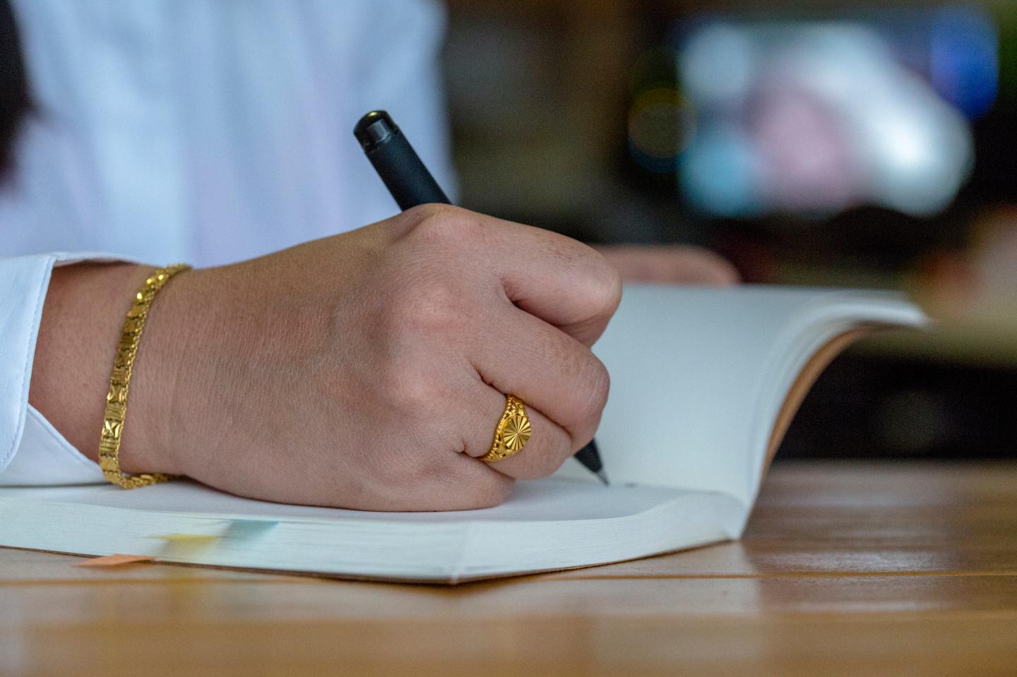A girl writes in a notebook, wearing gold ring and gold
