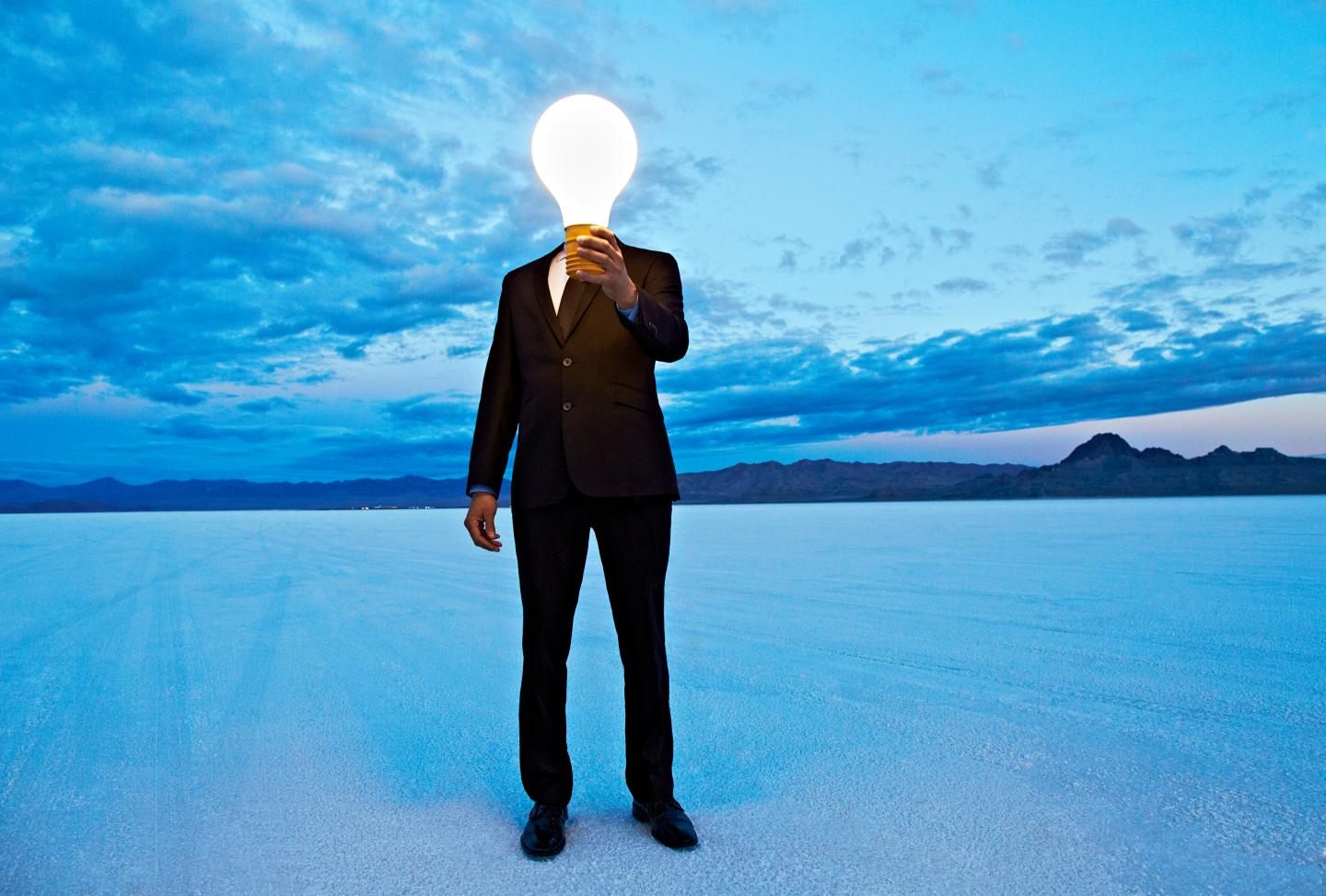 Man holding giant lightbulb in front of head.