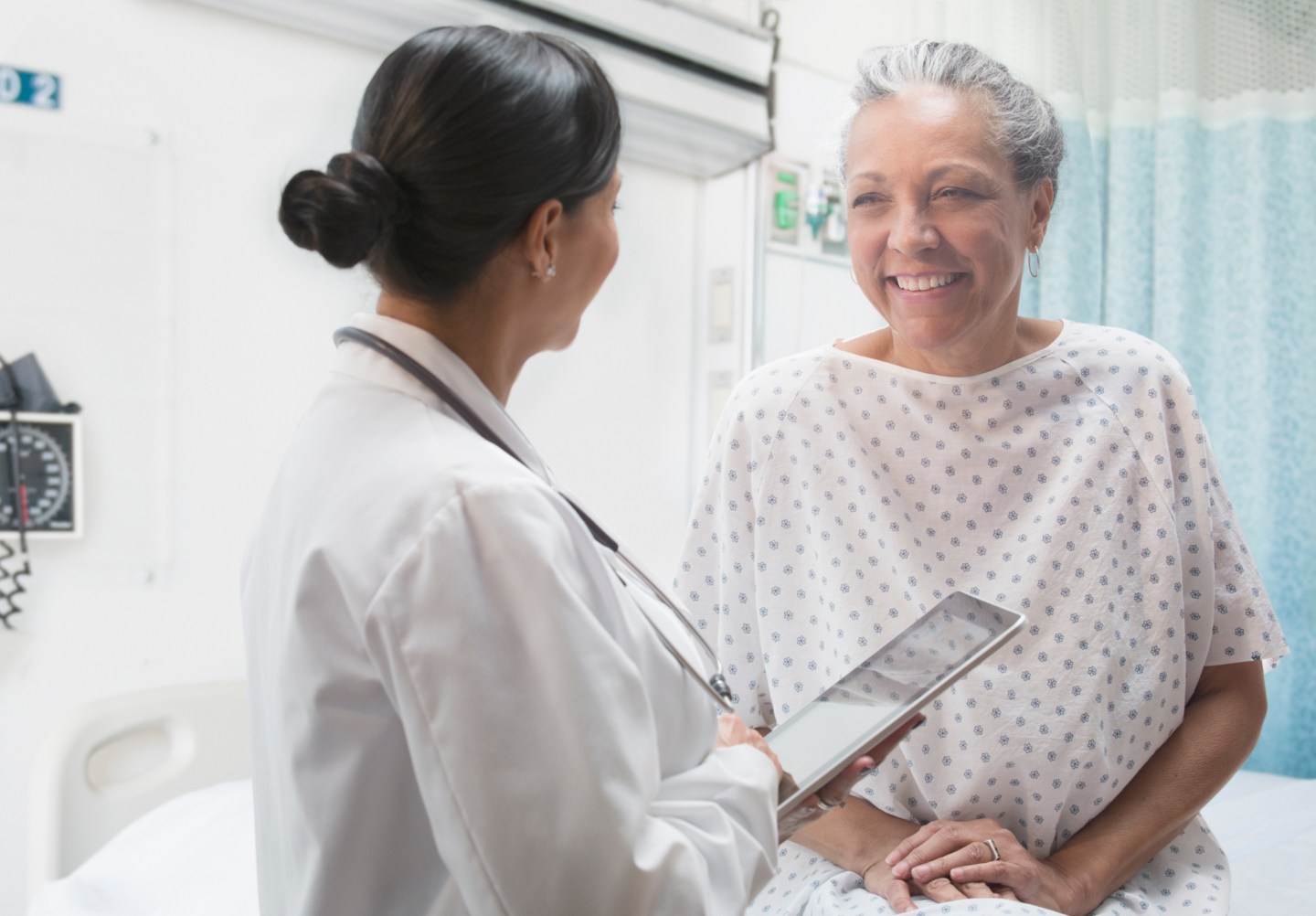 Hispanic doctor using digital tablet and talking to older patient