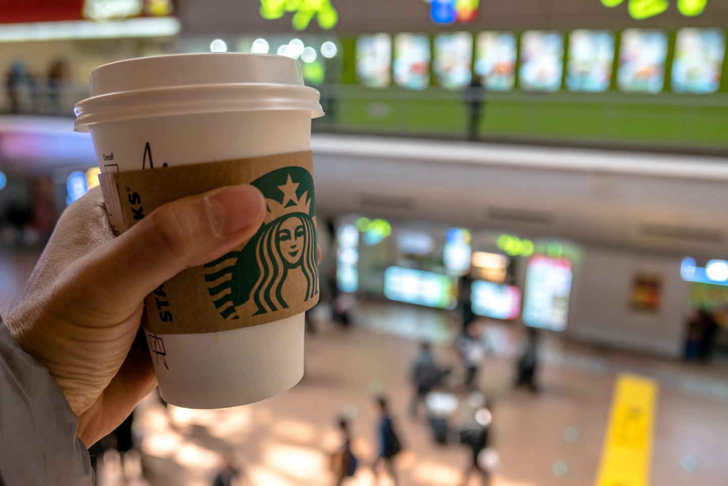 Hand holding a Starbucks coffee cup in a shopping area.